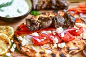 Venison steak souvlaki skewers on warm pita with homemade tzatziki, red bell peppers, red onion, diced tomatoes, and crumbled feta cheese.