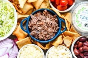 Greek Nachos with cooked and shredded goose meat, pita chips, tzatziki, kalamata olives, feta, mozzarella, red onion, shredded iceberg lettuce.