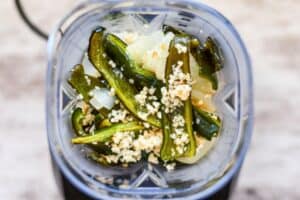 Roasted poblano peppers, onions, and garlic in a blender.