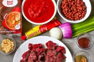 Steak Chili Recipe ingredients including deer steak, beef broth, onion, garlic, celery, crushed tomatoes, tomato paste, beans, and spices.