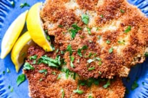 Schnitzel with chopped parsley and lemon wedges.