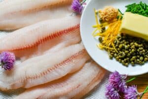 Walleye fillets with ingredients for lemon caper butter sauce, including butter, capers, fresh chives, and lemon zest