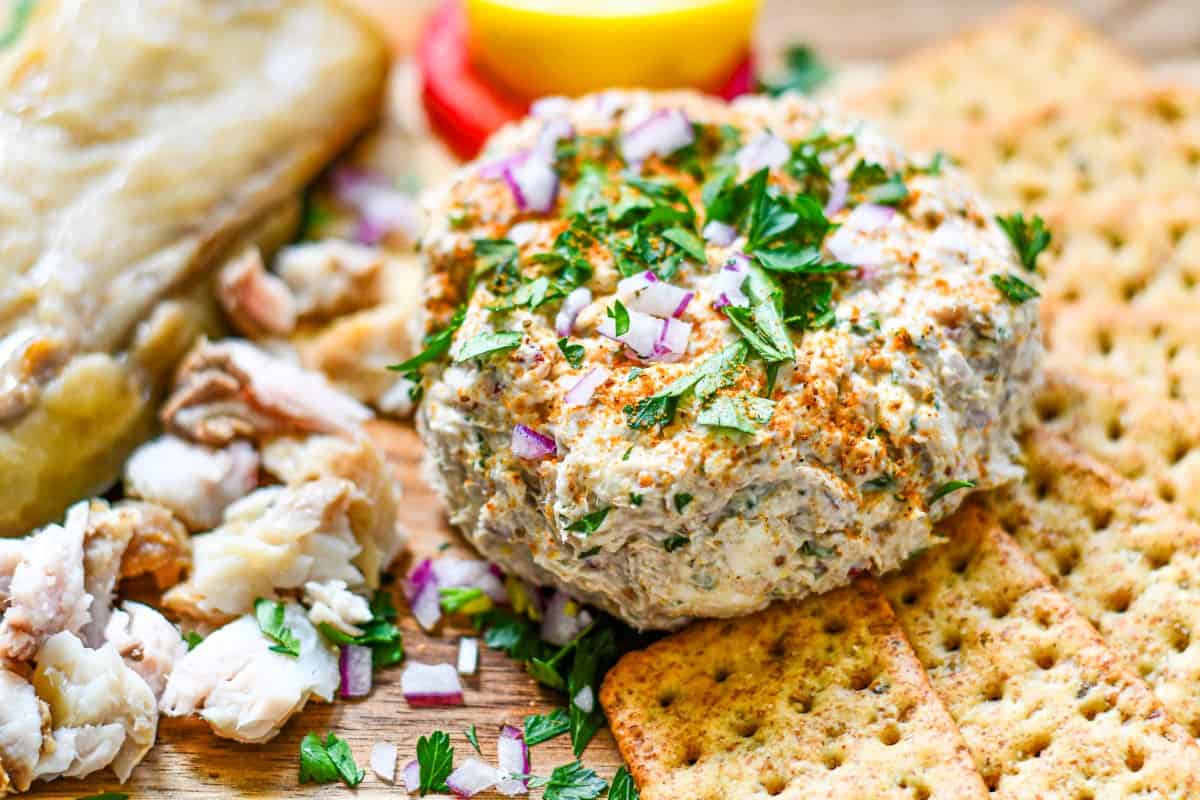 Smoked fish dip topped with red onion and parsley and served with crackers