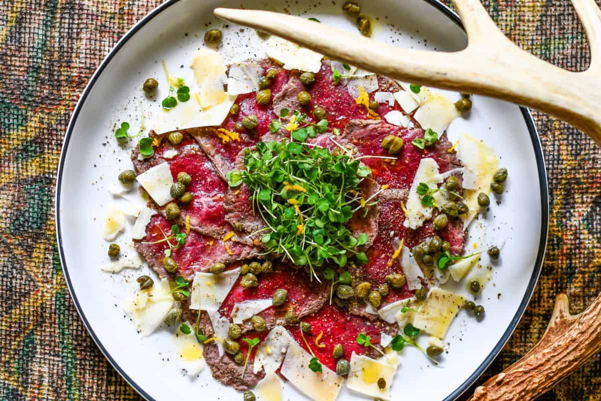 Venison carpaccio with baby arugula, capers, Parmesan, olive oil, lemon juice, and lemon zest